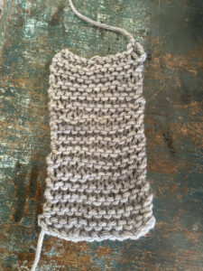A small grey piece of garter stitch. Starts wide and gets more narrow at the top.