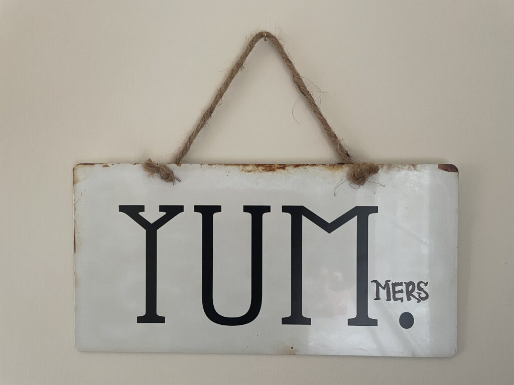wall sign that read "yum." but "mers" has been added to the end with marker so that the wign now reads "yummers"