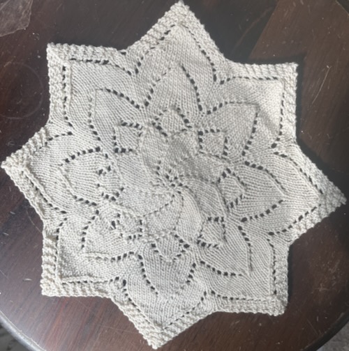 eight pointed lace doily (knit, flower motif in the middle) on a plain brown background